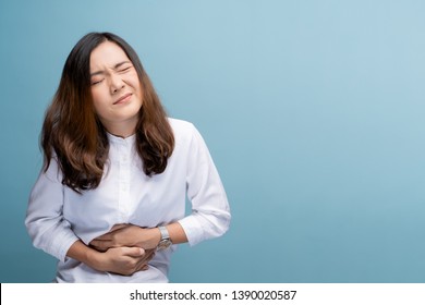 Woman has stomachache isolated over blue background - Shutterstock ID 1390020587