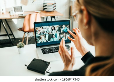 Woman has video call with her remote teammates using laptop.  White loft workspace