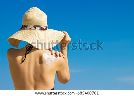 Woman in a hat applying sunscreen on her shoulder