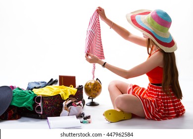 Woman In Hat Beside Suitcase. Girl Holds Piece Of Clothing. This One Is Too Small. Too Much Clothes In Luggage.