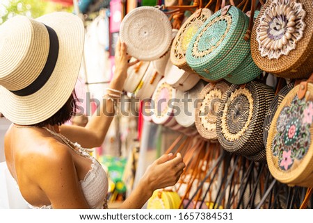 Woman in hat is coming to street market and choosing wicker handbag as souvenir from exotic country