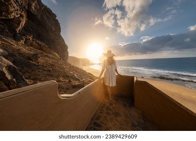 woman in a hat descending beach stairs at sunset, facing the ocean at Playa de Cofete, Fuerteventura, Canary Islands. - Powered by Shutterstock