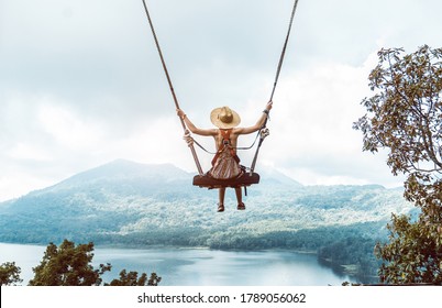 Woman with hat enjoying freedom on a swing in Bali, Indonesia. Life, adventure and peaceful feelings