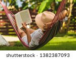 Woman with hat reading book in colorful hammock in tropical garden while relaxing in vacation.