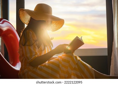 Woman in hat reading interesting book, travel guide books, novel with Rubber swim tube of heart shape while relaxing on floor at home. Sun shines on her from the big window with warm sunlight flare.  - Powered by Shutterstock