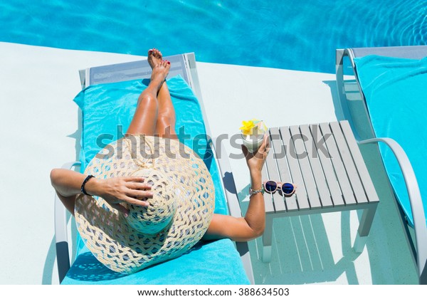 Woman in hat relaxing at the poolside with pina\
colada cocktail