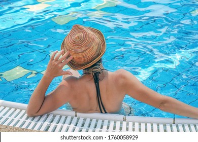 Mujer en esa piscina relajante a la vista trasera. Vista trasera. Mujer en sombrero en piscina de agua azul en el complejo.
