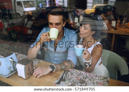 Woman in hat talking to man while he drinking cappuccino in cafe