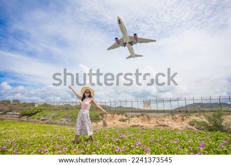 A woman in a hat walking on beach and beautiful Goat's Foot Creeper violet flower while the plane is taking off at Mai Khao beach, Phuket Thailand