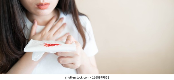 Woman Have A Coughing Up Blood And Chest Pain. Close Up Of Hands Holding Tissue Paper With Bloody Sputum. Cause Of Hemoptysis Include TB, Lung Cancer, Bronchitis, Pneumonia Or Pulmonary Embolism.