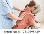 Woman having back and shoulders massage in medical office. Massage therapist massaging shoulders of woman sitting on massage chair 