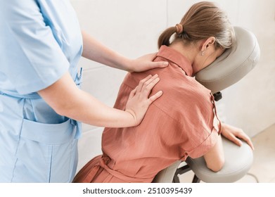 Woman having back and shoulders massage in medical office. Massage therapist massaging shoulders of woman sitting on massage chair  - Powered by Shutterstock