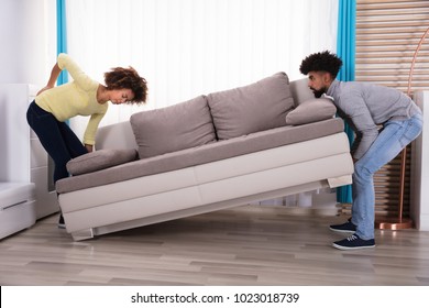 Woman Having Backpain While Lifting The Sofa With Her Husband In Living Room