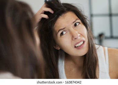 Женщина, имеющая плохой день волос grimacing в отвращении, как она смотрит в зеркало и бежит руки через ее волосы