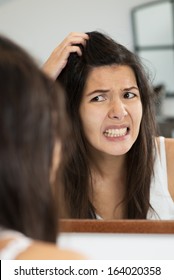 Woman Having A Bad Hair Day Grimacing In Disgust As She Looks In The Mirror And Runs Her Hands Through Her Hair