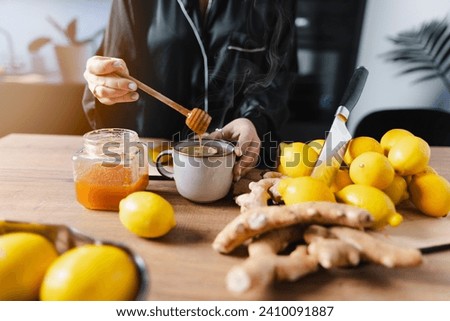 A woman is having a cup of tea on a beautiful morning. Adding honey to the tea with a honey dipper.
