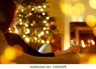 Woman Having A Drink By A Fireplace In A Cozy Dark Living Room On Christmas Eve