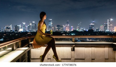 Woman having a drink on roof terrace overlooking the city skyline