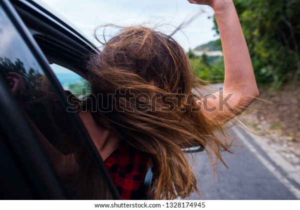 Woman is having fun in a car drive, enjoying a\
cloudy day and a beautiful\
nature