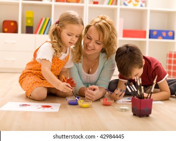 Woman having fun with kids laying on the floor painting hands-focus on the girl face