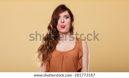 Woman having fun, making silly face sticking tongue studio shot on yellow