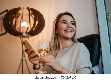 Woman having a glass of wine while using her phone. - Powered by Shutterstock