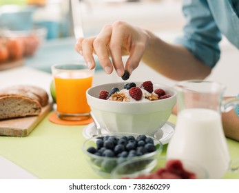 Woman Having An Healthy Delicious Breakfast At Home With Yogurt, Cereals And Fresh Fruit, She Is Picking A Blueberry