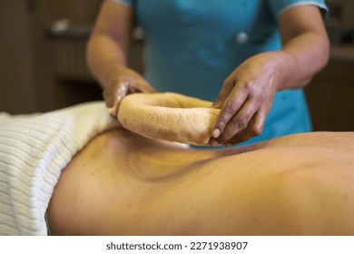 Woman having kati vasti Ayurveda treatment in spa while warm oil placing on her back