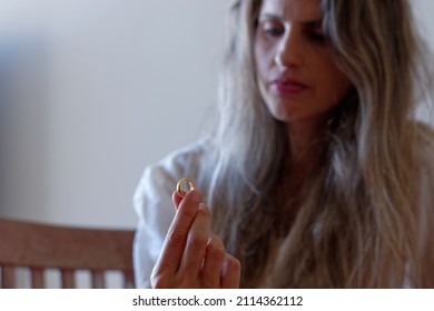 Woman Having Second Thoughts About Her Marriage Holding And Looking At Her Wedding Ring.