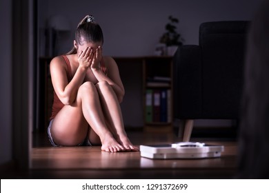 Woman having stress about weight loss, diet or gaining weight. Eating disorder, anorexia or bulimia concept. Young girl crying and sitting on the floor with scale. Underweight person sad about obesity