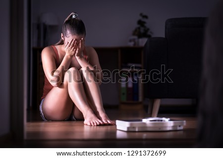 Woman having stress about weight loss, diet or gaining weight. Eating disorder, anorexia or bulimia concept. Young girl crying and sitting on the floor with scale. Underweight person sad about obesity