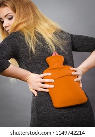 Woman having strong back pain holding hot red water bottle on her spine. Health care, remedy for pains concept