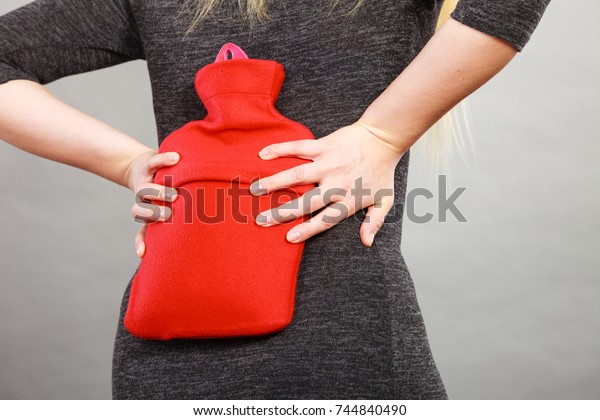 Woman having strong\
back pain holding hot red water bottle on her spine. Health care,\
remedy for pains concept