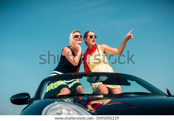 Woman having summer trip in convertible car\
stretching hands in the air with\
fun