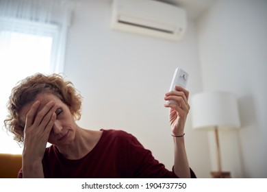 Woman With Headache Using Aircondition Unit At Home.