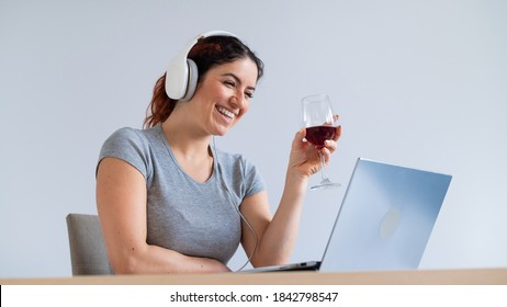 A Woman In Headphones Drinks Red Wine And Communicates With Friends Via Video Communication On A Laptop. Online Chat In Quarantine