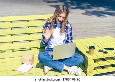 Woman With Headphones Having A Facetime Video Call With Laptop Outside. Happy And Smiling Girl Working And Drinking Coffee. Using Computer. Distance Learning Online Education And Work.