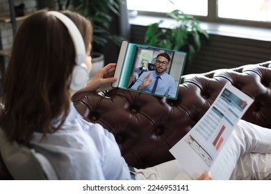 Woman in headphones lying on sofa speak talk on video call with colleagues on online briefing on digital tablet. Transparent modern touchpad of the future concept - Powered by Shutterstock