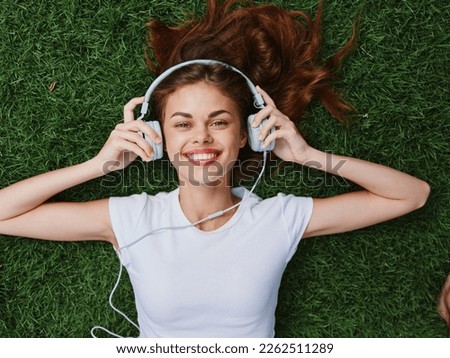 Woman in headphones portrait lying on the grass and listening to music looking at the camera smile and happiness