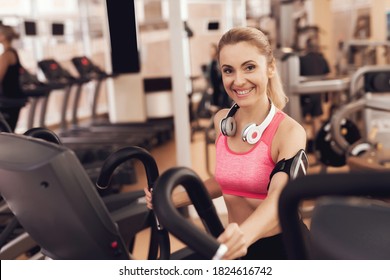 Woman With Headphones In Sportswear Running On Treadmill At The Gym. Young Sports Girl On The Simulator Does Exercises In The Gym. 