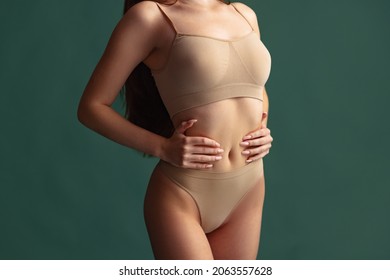 Woman health care, motherhood. Portrait of slim female body in beige underwear isolated over green background. Concept of beauty, body and skin care, health, cosmetics, spa. Copy space for ad.
