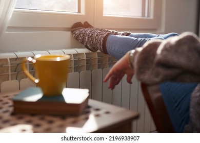 Woman heating feet on a chilly winter day, energy and gas crisis, cold room, heating problems. - Shutterstock ID 2196938907