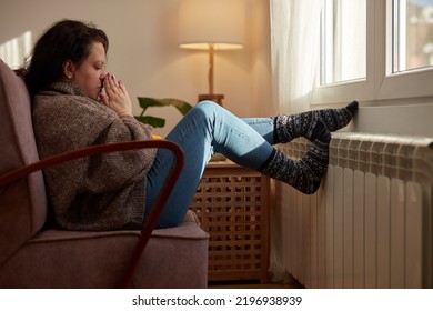 Woman heating feet on a chilly winter day, energy and gas crisis, cold room, heating problems. - Shutterstock ID 2196938939