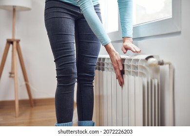 Mujer calentando sus manos en el radiador durante los fríos días de invierno.