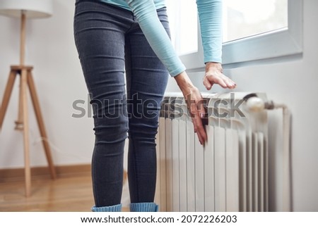 Woman heating her hands on the radiator during cold winter days.