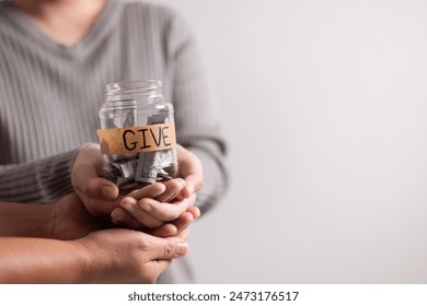 Woman held jar filled with cash with words in bold lettering urging people to donate money, extending her hand in gesture of giving part of her business's charitable efforts.
