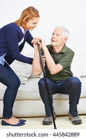 Woman helping senior man with cane getting up from sofa at home - Shutterstock ID 445842889