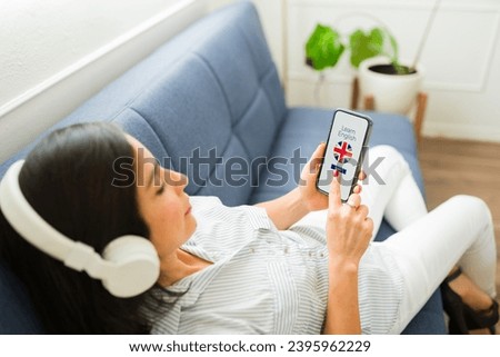 Woman in her 30s relaxing on the sofa with headphones using the online app on her smartphone to learn English in the UK 