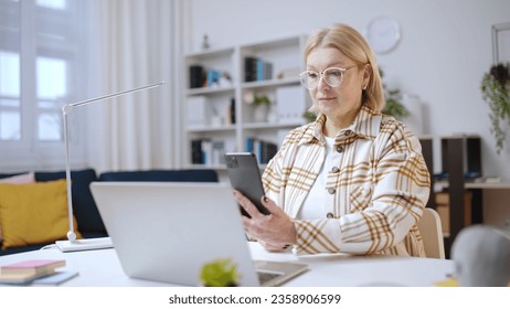 Woman in her 50s using smartphone to make a purchase, scanning qr code on laptop - Powered by Shutterstock