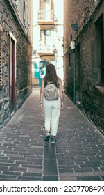 Woman With Her Back Turned Walking Down A Street In An Old Village